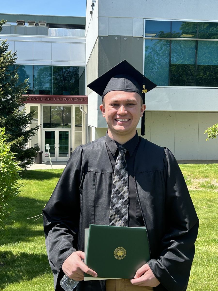 Alex smiling in his graduation cap and gown, holding his diploma
