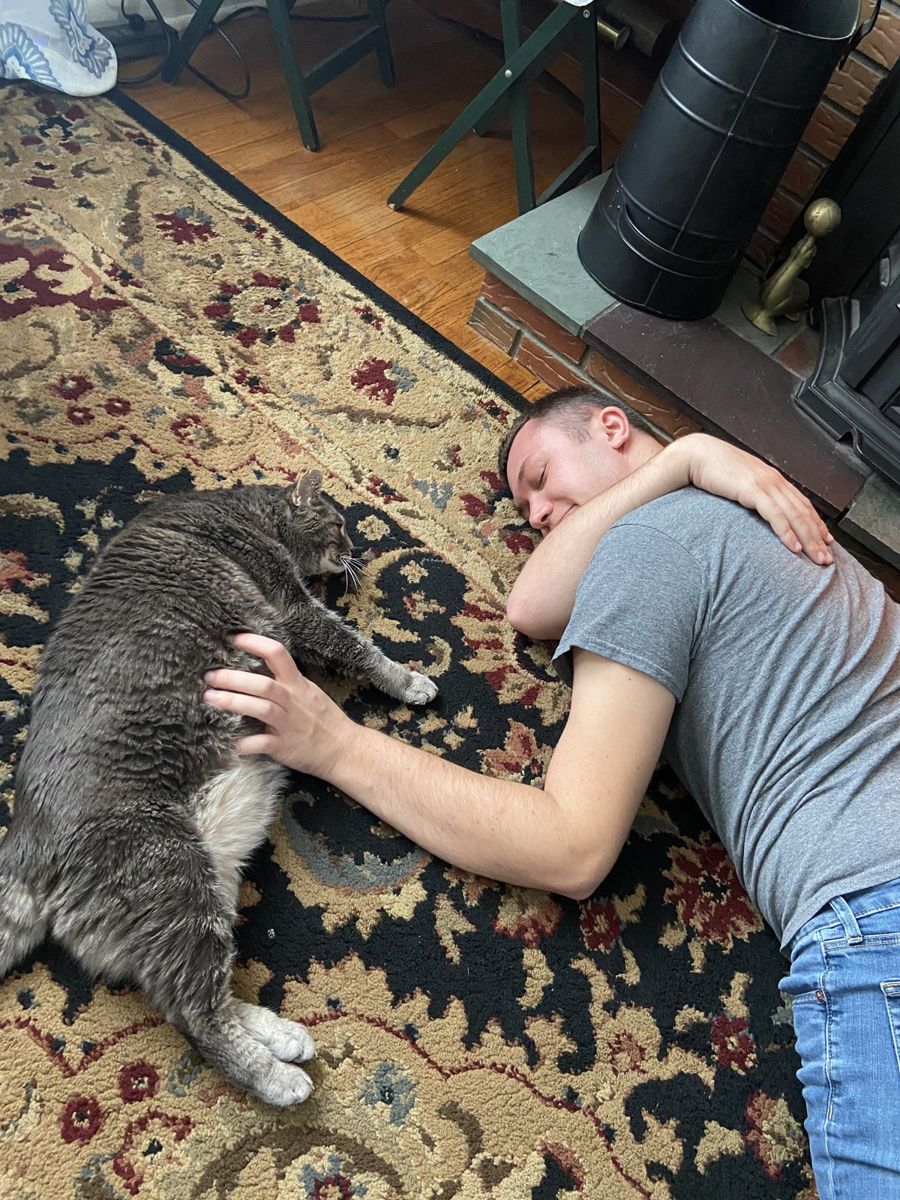 Alex lying on the rug at home, cuddling a gray cat